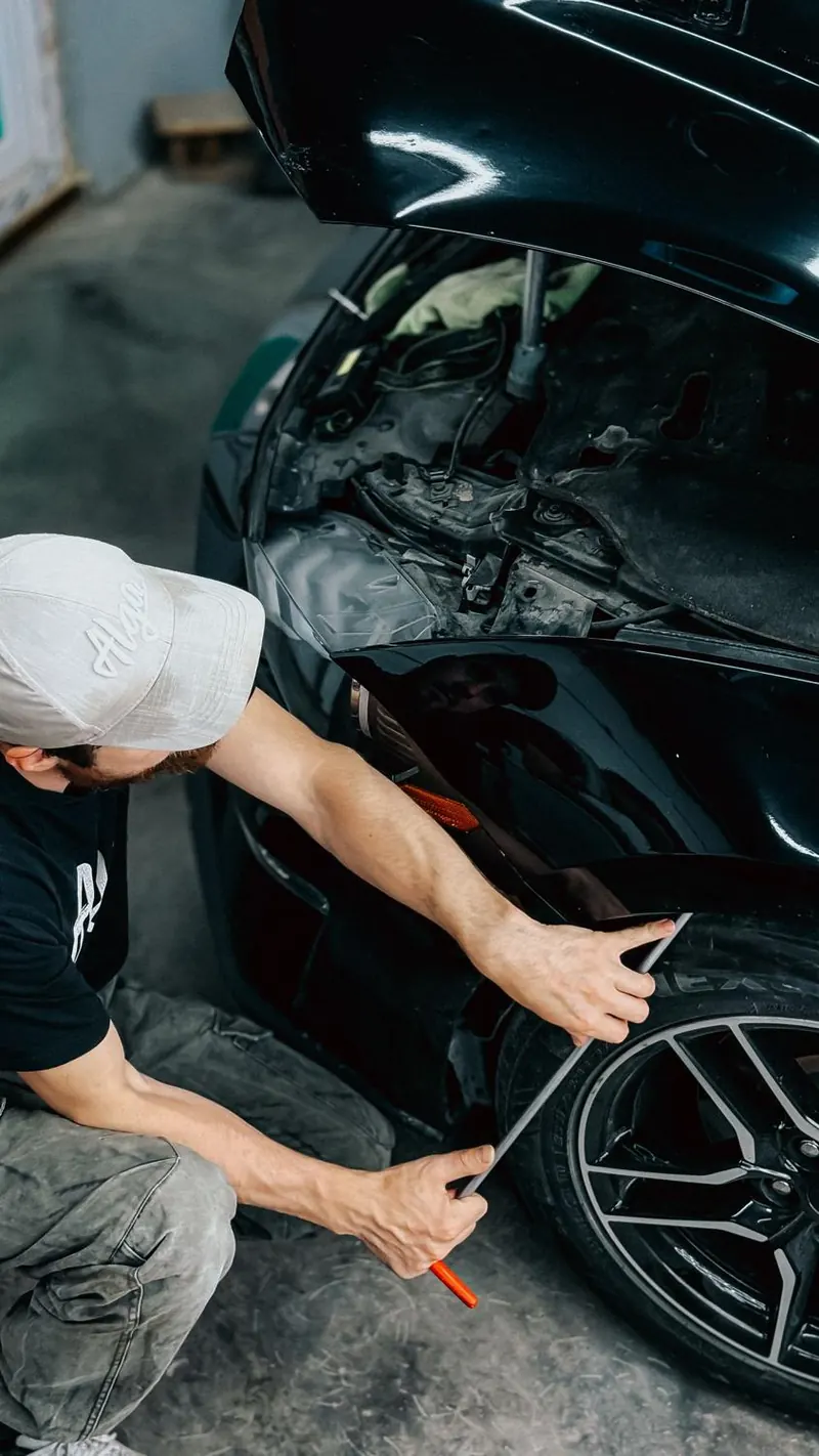Hombre agachado reparando la carrocería de un auto negro